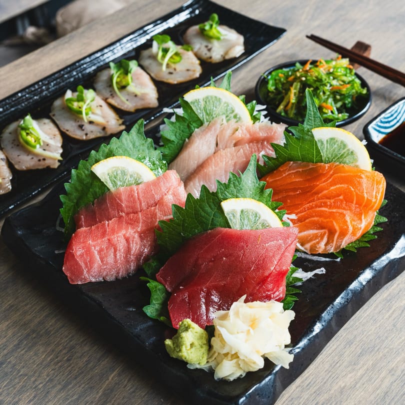 A platter of fresh tuna and salmon sashimi, garnished with lemon, shiso leaves, wasabi, and ginger.