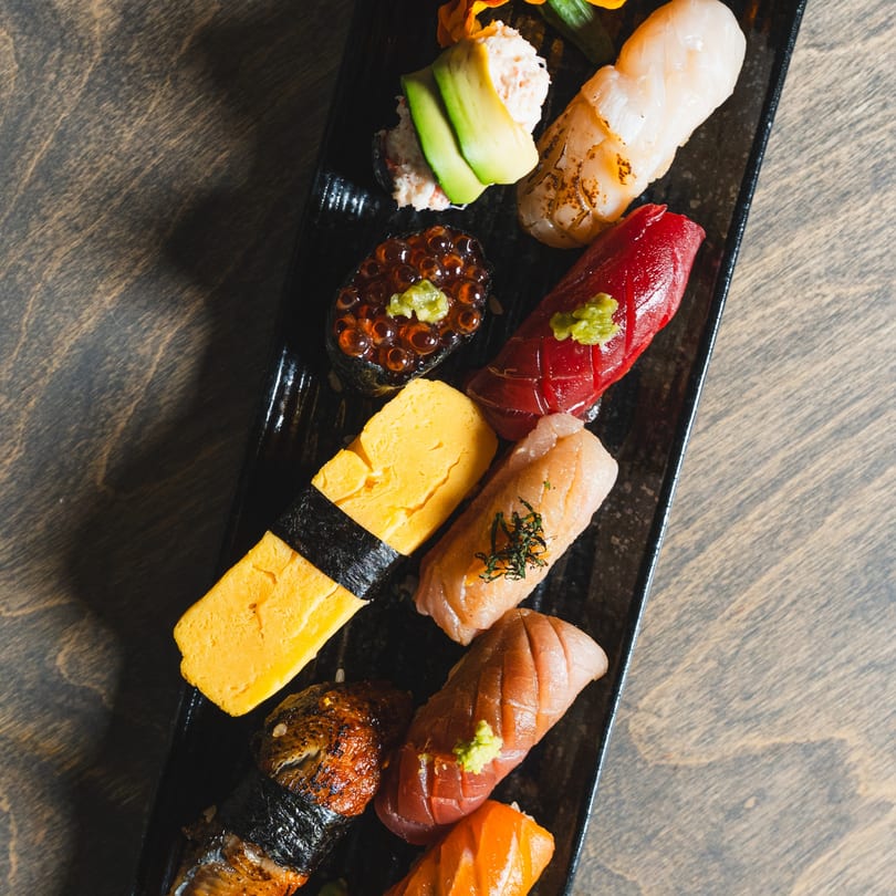 Assorted nigiri and gunkan sushi with various toppings, including tuna, salmon, and roe, on a black plate.